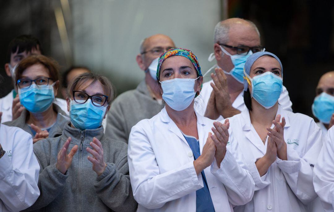 Varios profesionales sanitarios aplauden a las puertas de un hospital.