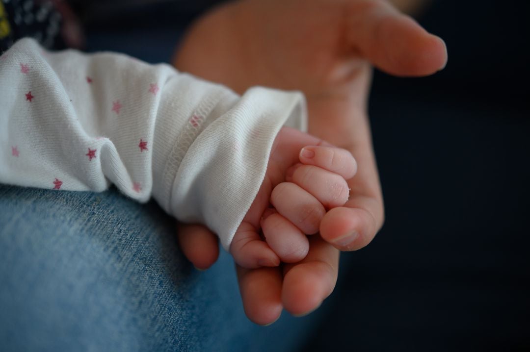 Una mujer sostiene la mano de su hijo de dos semanas de edad.