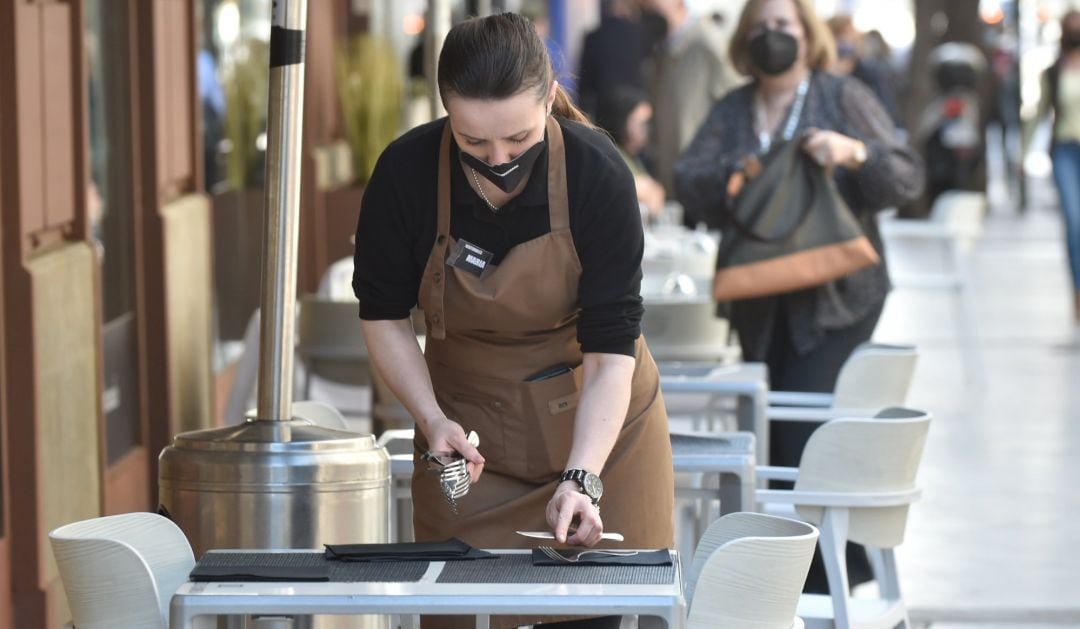 Una camarera preparando las mesas de una terraza.