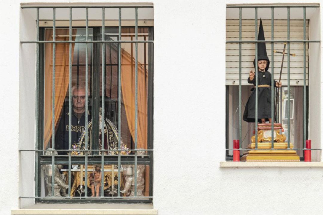 Un hombre se asoma desde la ventana de su casa en Sevilla en la pasada Semana Santa. en una de las ventanas, una dolorosa, en otra, un niño Jesús vestido de nazareno