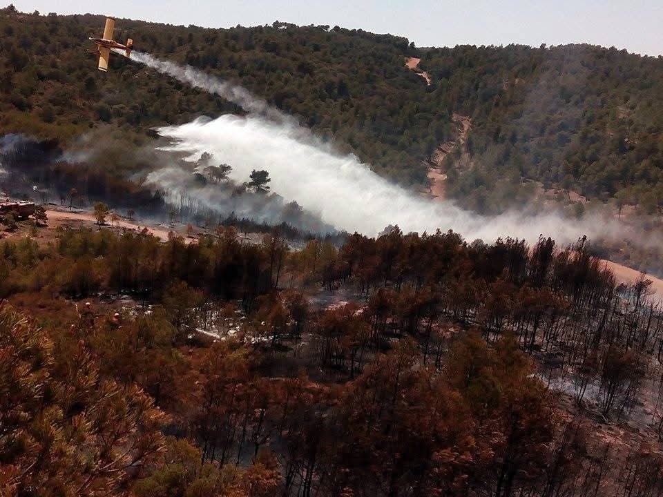 Un avión de extinción descarga agua sobre la zona afectada por el incendio forestal en la Sierra Mariola, en Bocairent