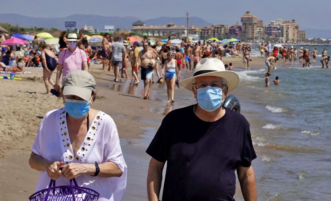 Dos personas pasean, este domingo, por la orilla de la playa de La Patacona de Alboraia protegidos con mascarillas