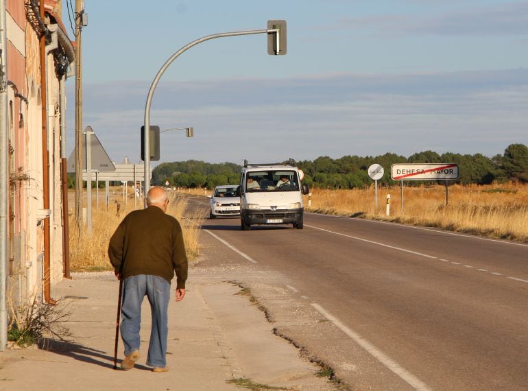 Un mayor pasea en la acera paralela a la carretera mientras se acercan dos vehículos