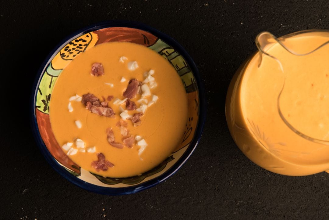 Cuenco con salmorejo con trozos de huevo duro y jamón y jarra con salmorejo