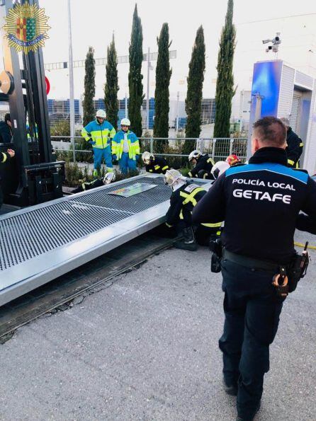 Policía de Getafe y Bomberos de la Comunidad de Madrid rescatando al hombre atrapado bajo una puerta metálica.