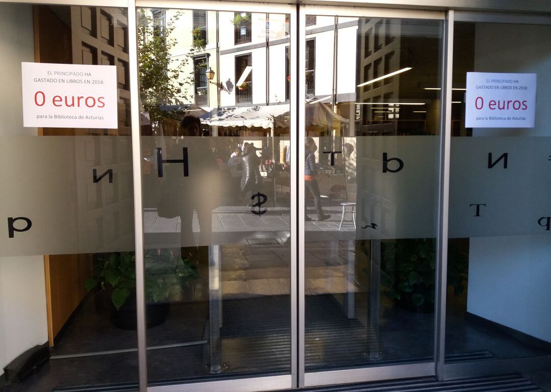 La puerta de la Biblioteca de Asturias &quot;Ramón Pérez de Ayala&quot;, en El Fontán, Oviedo, con los carteles de protesta por la falta de inversión en libros del Principado.