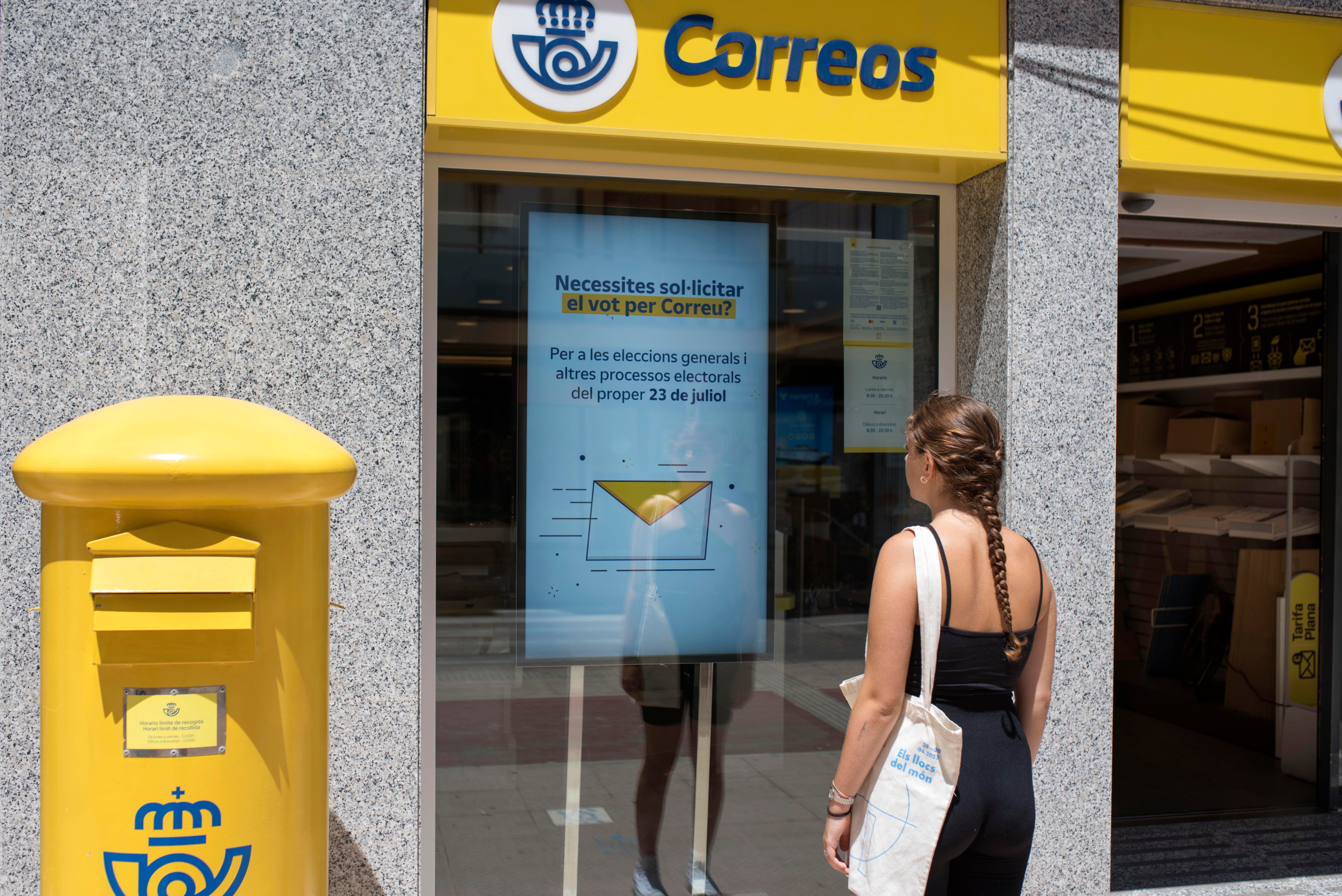 Una mujer observa la información sobre el voto por correo en una oficina de Menorca.