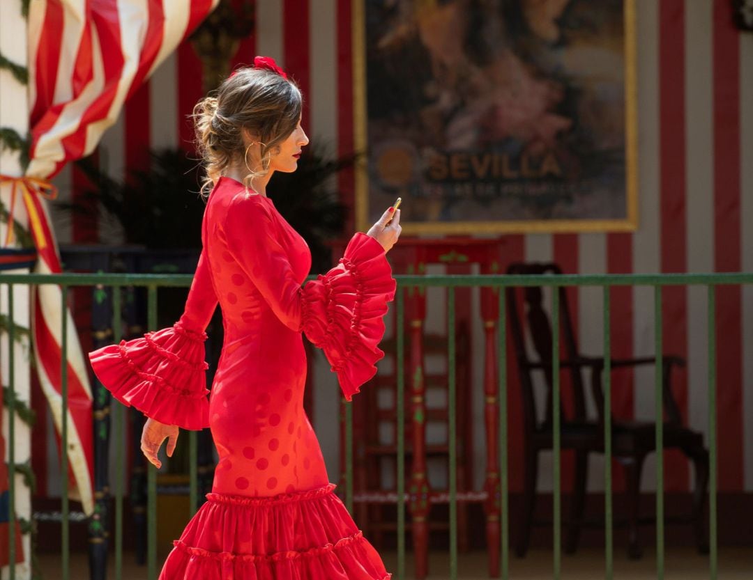 Una mujer vestida de flamenca pasa junto a una de las casetas en el Real de la Fería de Abril de Sevilla. EFE. Raúl Caro