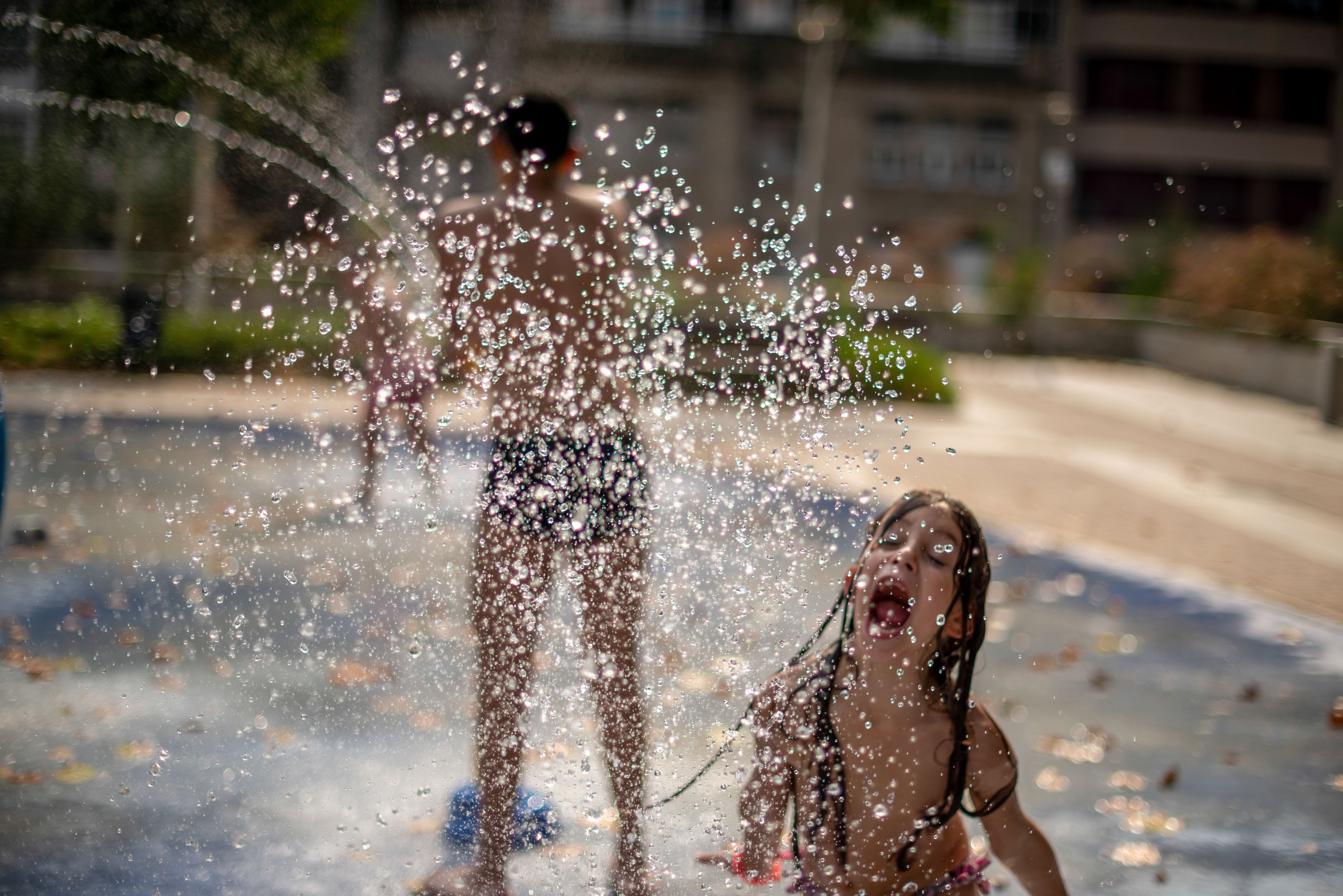 Varios niños se refrescan con una fuente de un parque público, este jueves en Ourense.