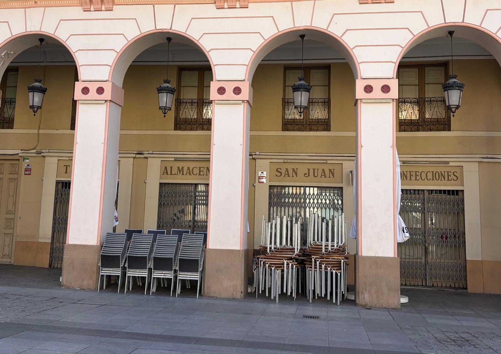 Mesas y sillas apiladas bajo los arcos de la plaza de López Allué