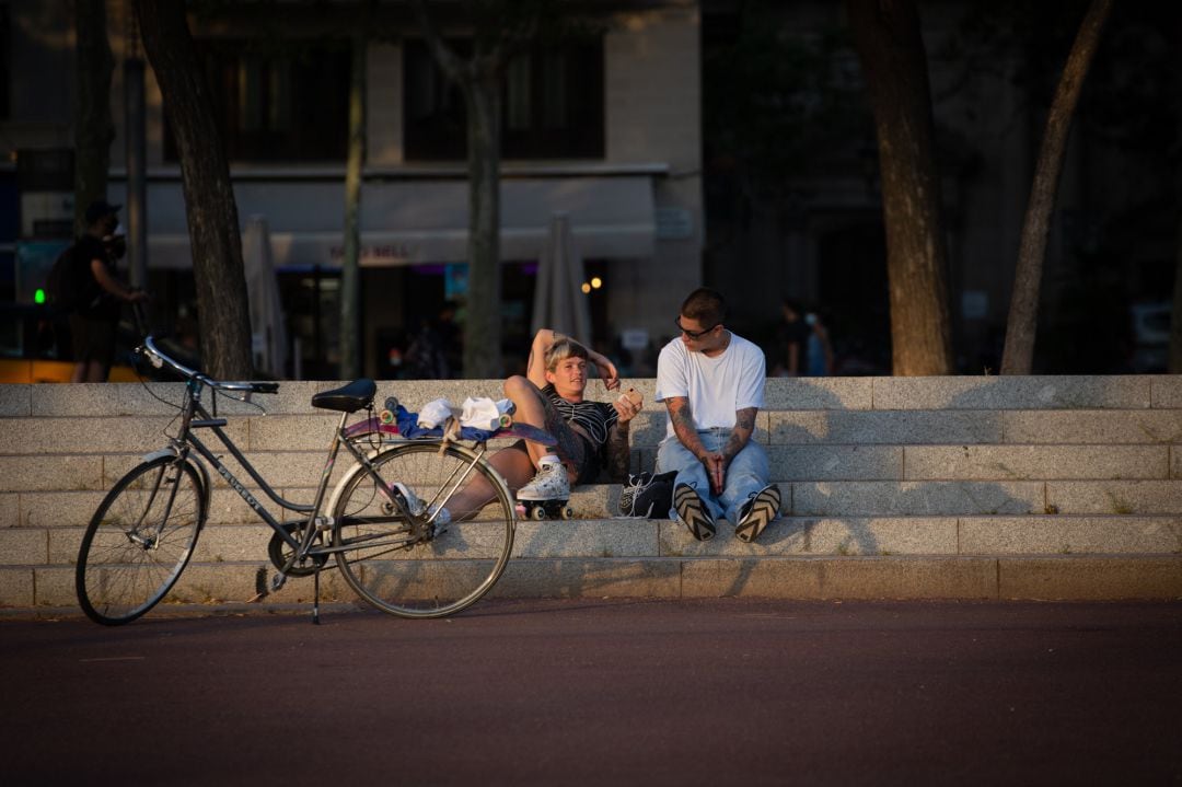 Dos jóvenes descansan junto a una bicicleta en Barcelona.