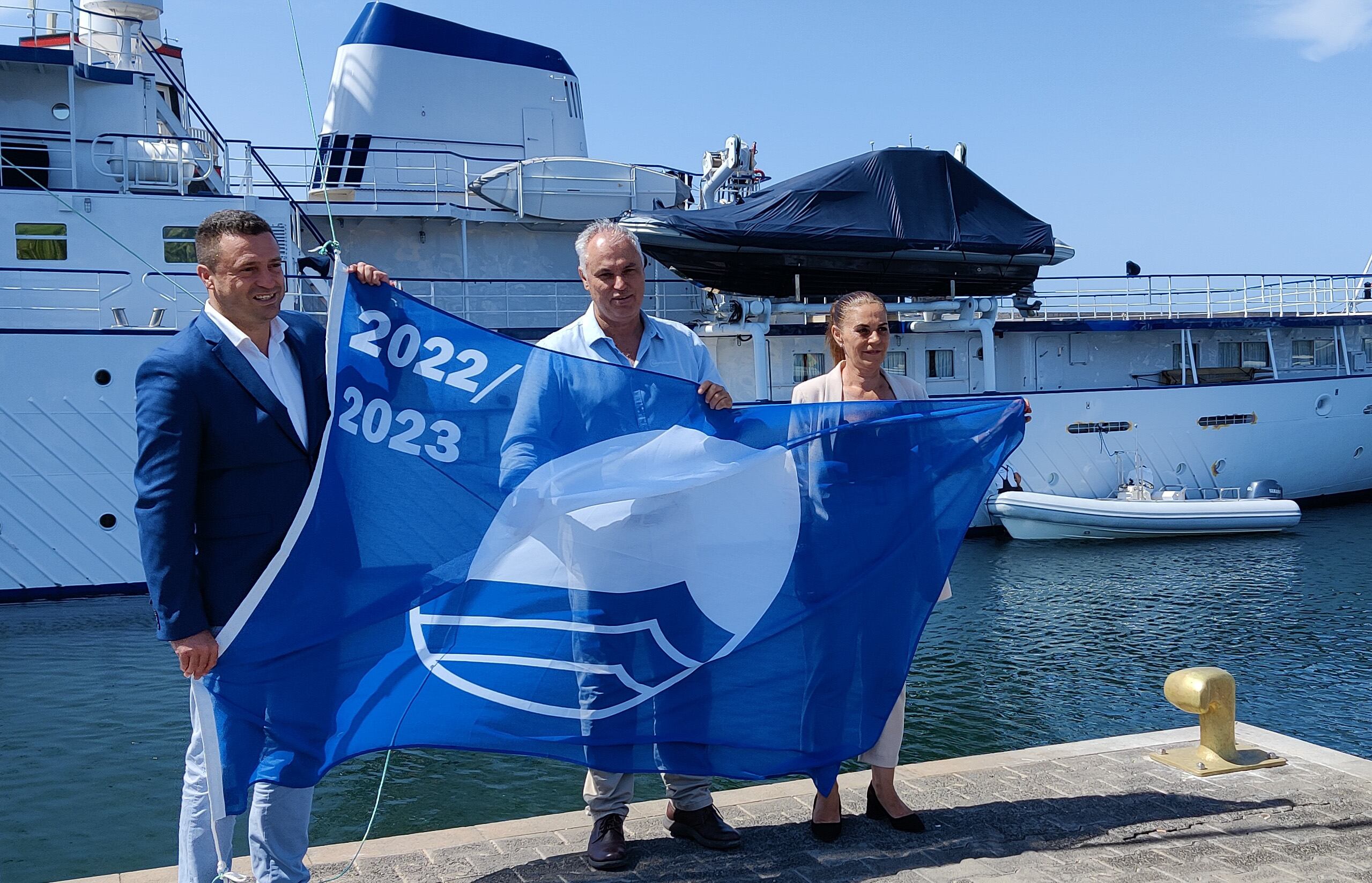 El alcalde de Yaiza,  Oscar Noda, la concejal de desarrollo local y playas, Fátima Viñoly y el director de operaciones de Calero Marinas, Constante Lorenzo, izando la bandera azul.