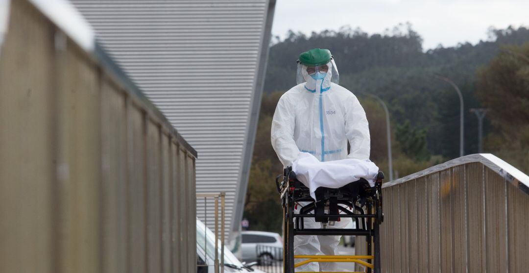 Archivo - Un trabajador sanitario totalmente protegido traslada una camilla en las inmediaciones de la residencia de ancianos