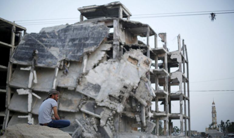 A Palestinian shepherd herds livestock as a man sits near residential buildings, that witnesses said were heavily damaged by Israeli shelling during a 50-day war last summer, in Beit Lahiya town in the northern Gaza Strip May 25, 2015. REUTERS/Suhaib Sale