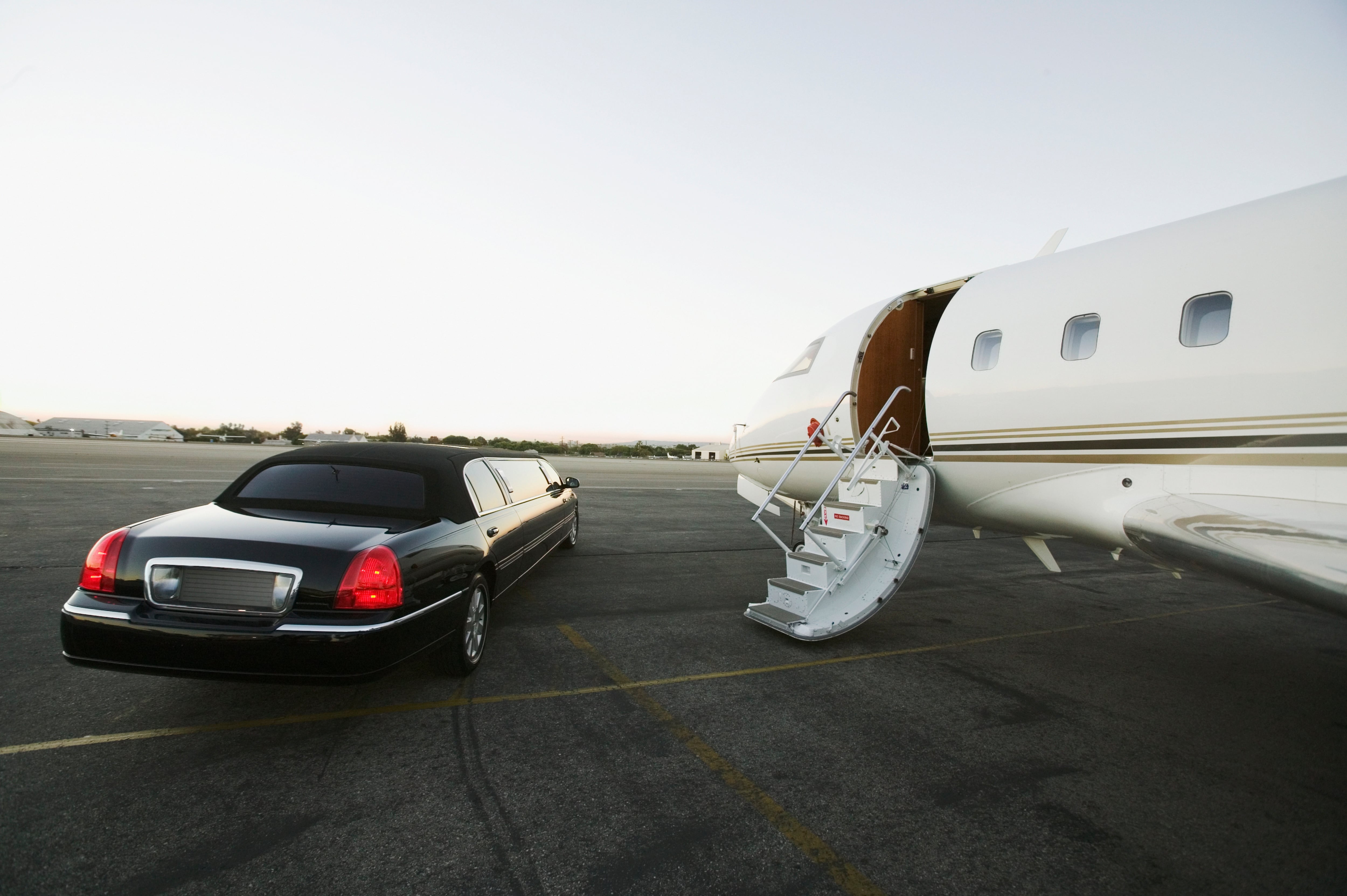 Una limusina en la pista de un aeropuerto frente a un jet privado