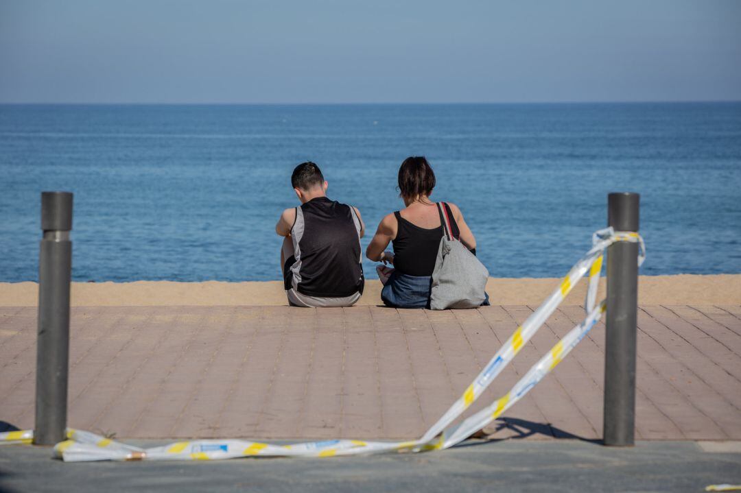 Dos jóvenes sentados en el Paseo Marítimo de la Playa de la Barceloneta 