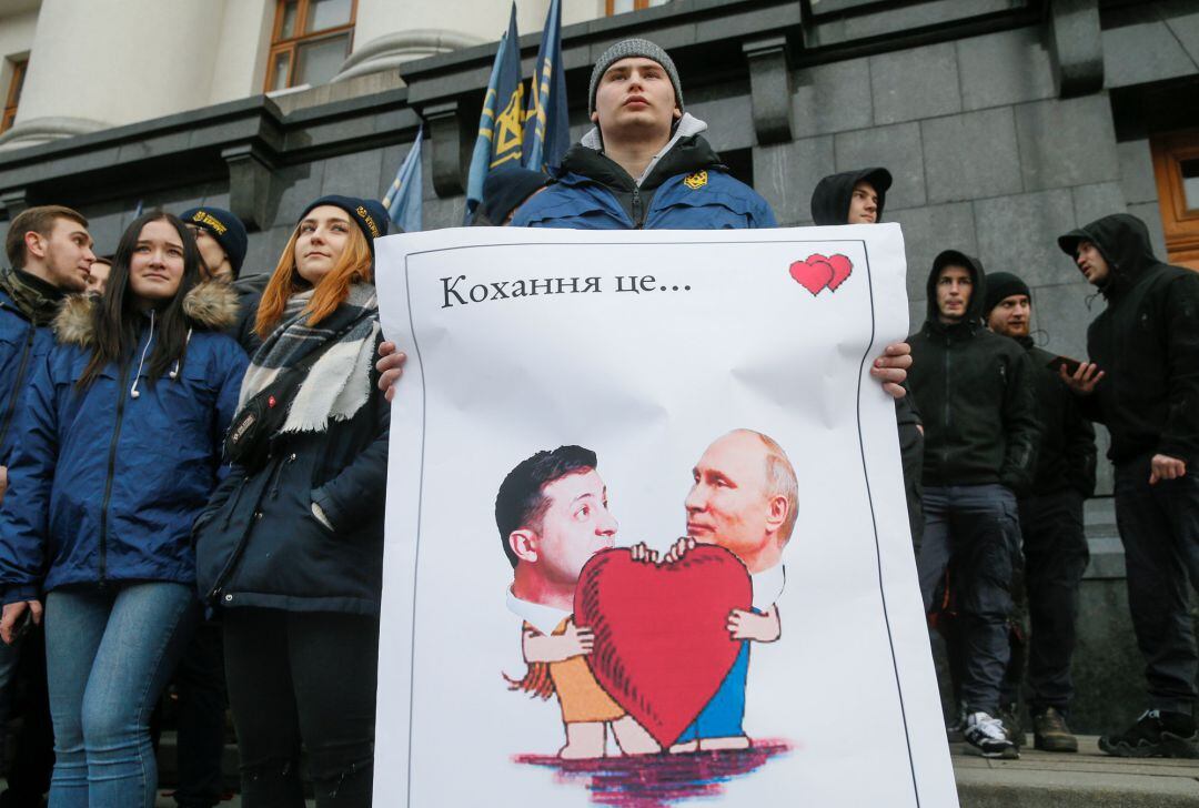 Un manifestante sostiene un póster que representa al presidente ucraniano Volodymyr Zelenskiy y al presidente ruso Vladimir Putin durante una protesta de activistas y simpatizantes de un partido político del Cuerpo Nacional frente al edificio de la Administración Presidencial en el Día de San Valentín en Kiev. El cartel dice: &quot;Amor es...&quot;