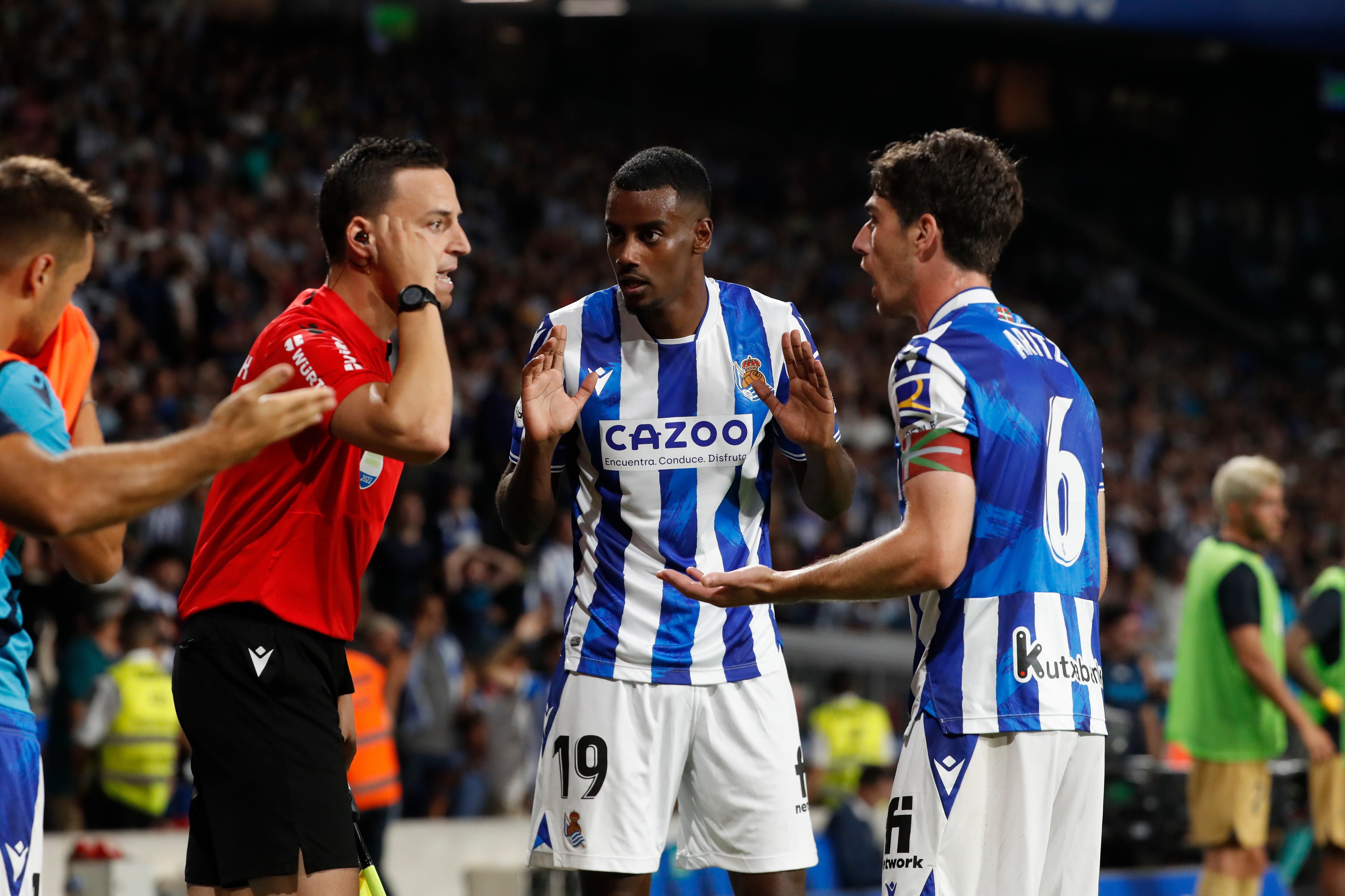 SAN SEBASTIÁN, 21/08/2022.- El árbitro Munuera Montero (i) conversa con Aleksar Isak (c) y Aritz Elustondo, ambos de la Real Sociedad, durante el partido de Liga en Primera División ante el FC Barcelona que disputan este domingo en el Reale Arena, en San Sebastián. EFE/Javier Etxezarreta