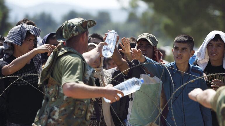 Un soldado reparte agua entre los inmigrantes que esperan en el paso fronterizo de Macedonia y Grecia cerca de Gevgelija hoy, 28 de agosto de 2015