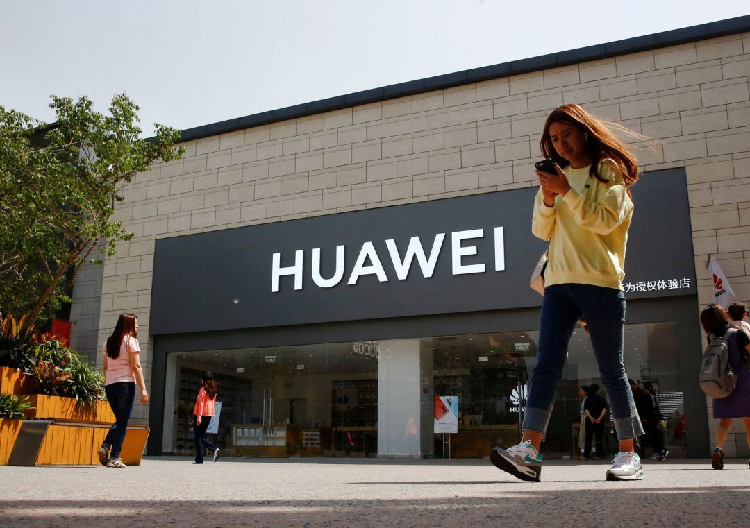 Una mujer mira el teléfono frente a una tienda de Huawei.