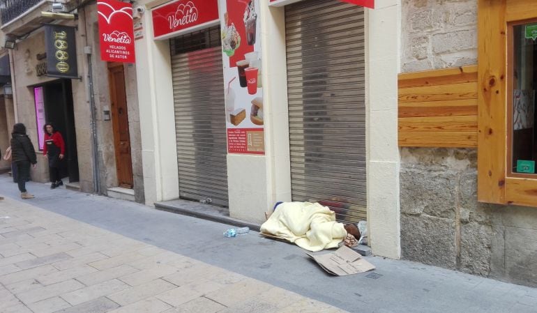 Una persona sin hogar duerme cobijado en un establecimiento en pleno centro de Alicante.