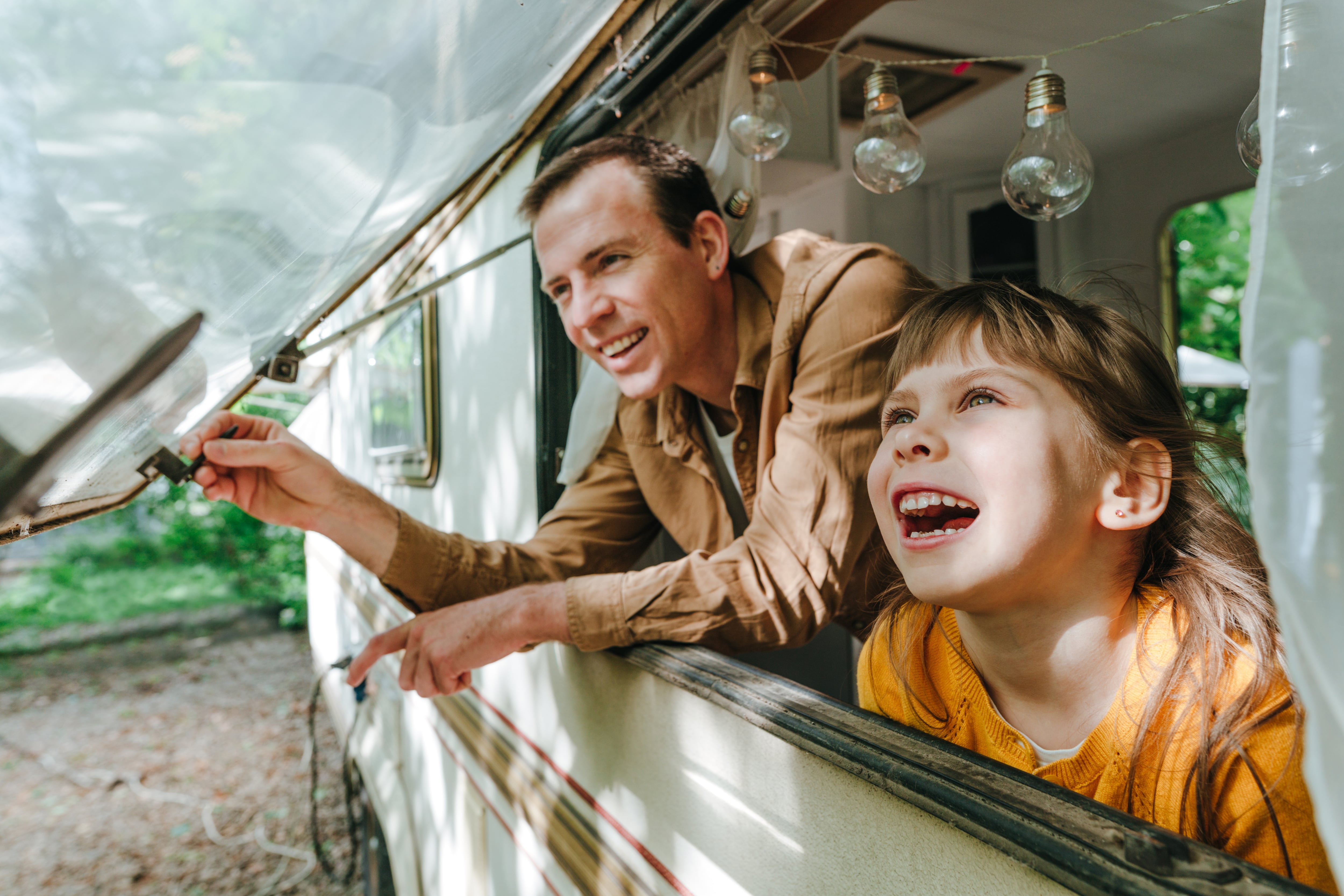 Un padre y su hija en la ventana de la caravana en la que acampan. Recurso.