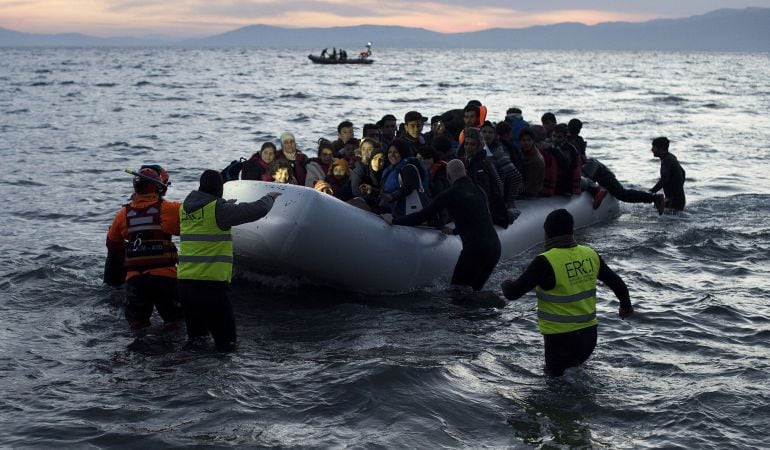 Voluntarios y salvavidas remolcan un bote de refugiados a su llegada a Lesbos