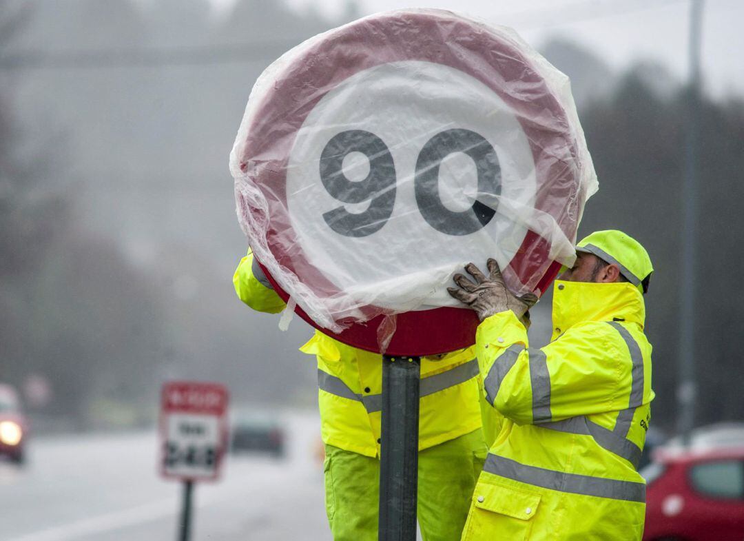 Adiós a los 100 kilómetros por hora en las carreteras convencionales. En la imagen, dos operarios realizan el cambio de señalización, la cual han sustituido por la nueva limitación a 90 kmh,