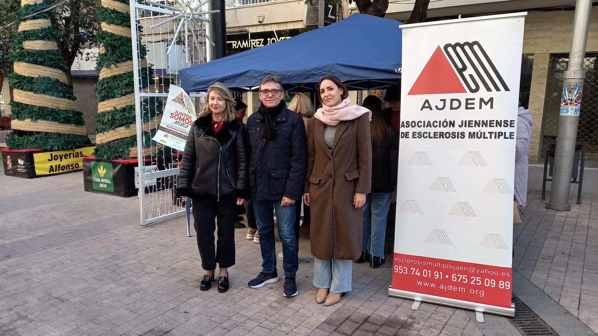 Personalidades del Ayuntamiento de Jaén y AJDEM posan delante del stand durante el Día Mundial de la Esclerosis Múltiple