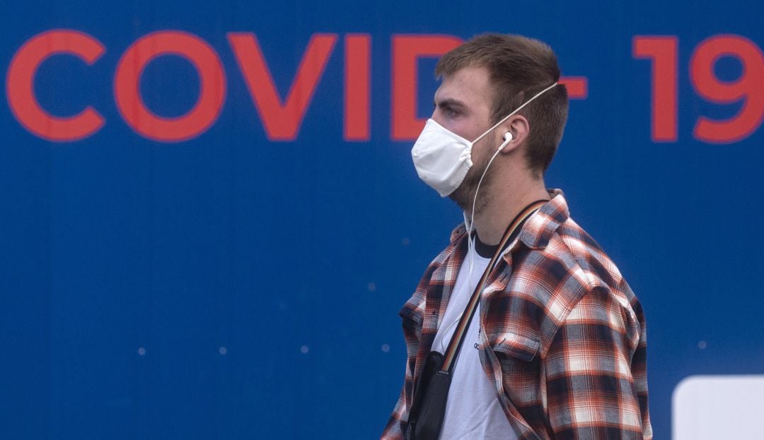 Un joven camina con una mascarilla puesta.