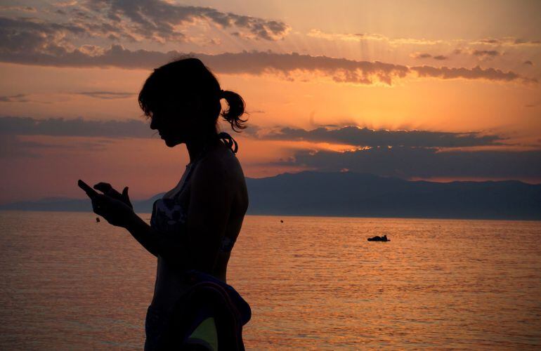 Una mujer revisa su móvil en la playa.