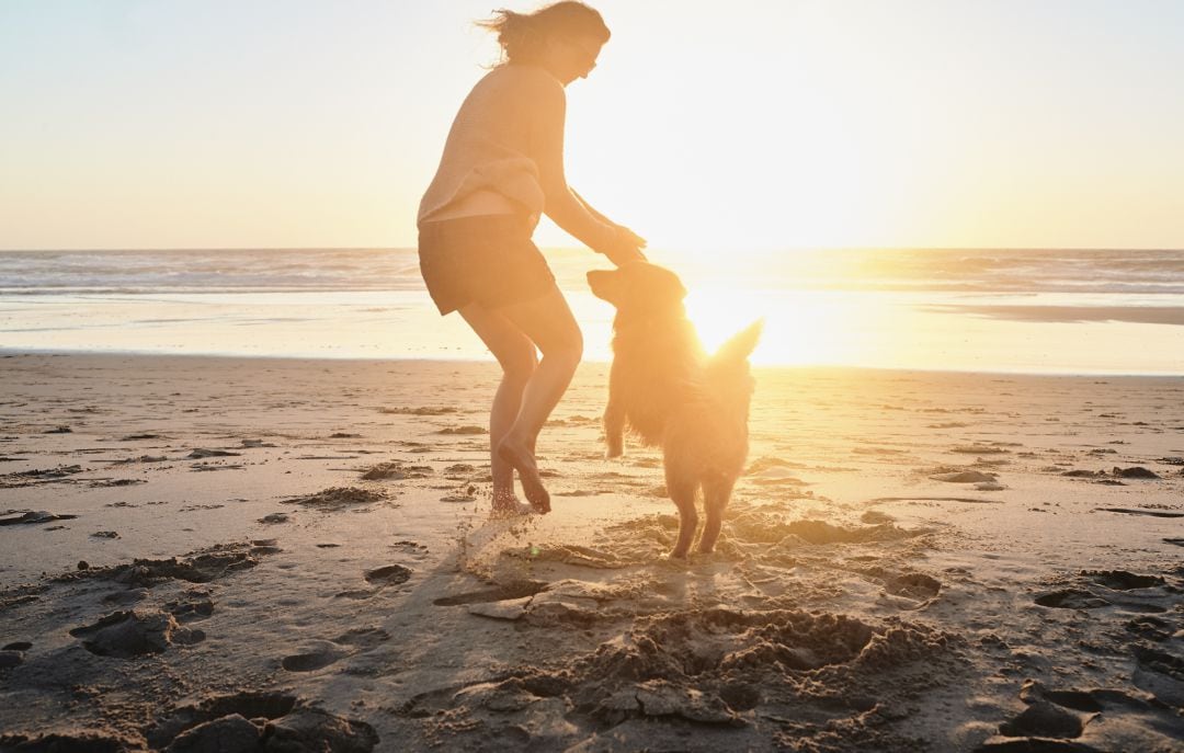 Una mujer en la playa junto a su perro.