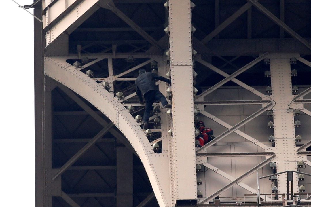 Un hombre escala la Torre Eiffel mientras varios bomberos tratan de detenerlo, este lunes en París (Francia