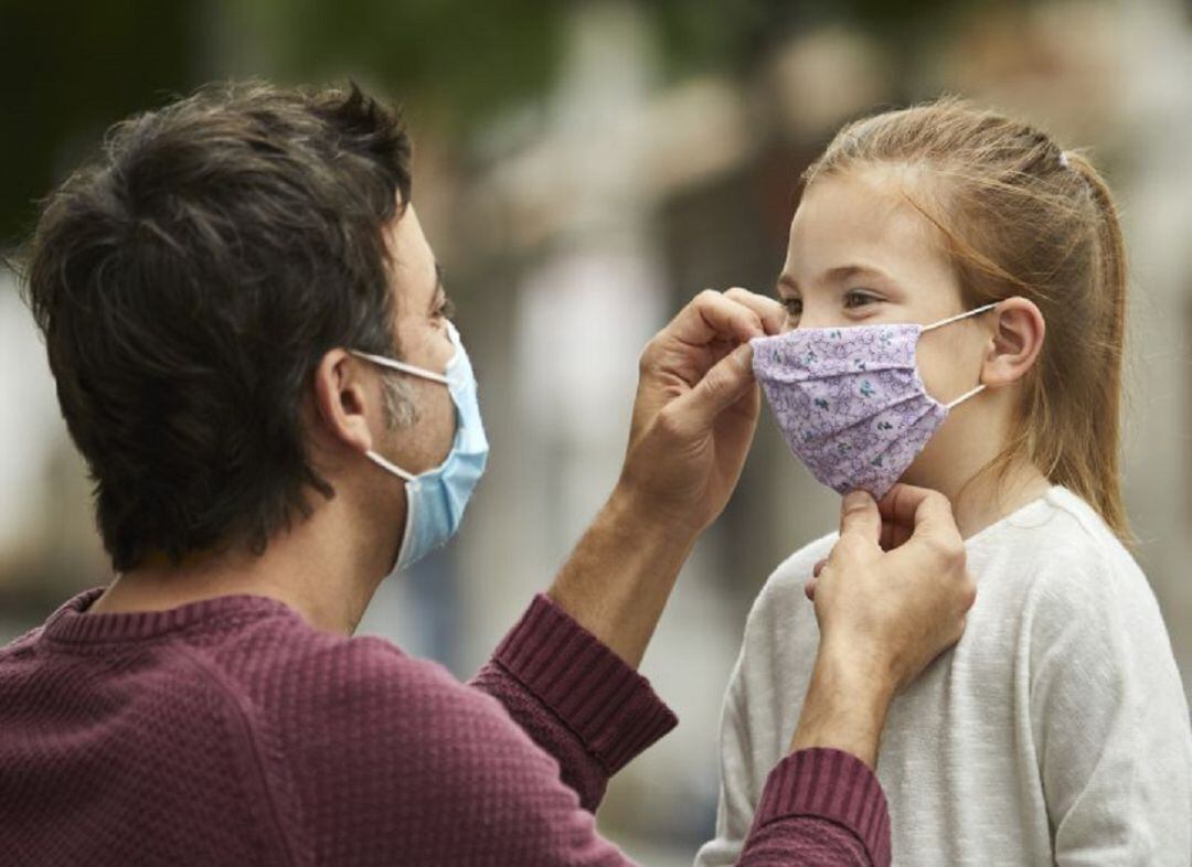 Un padre ayuda a su hija a colocarse la mascarilla