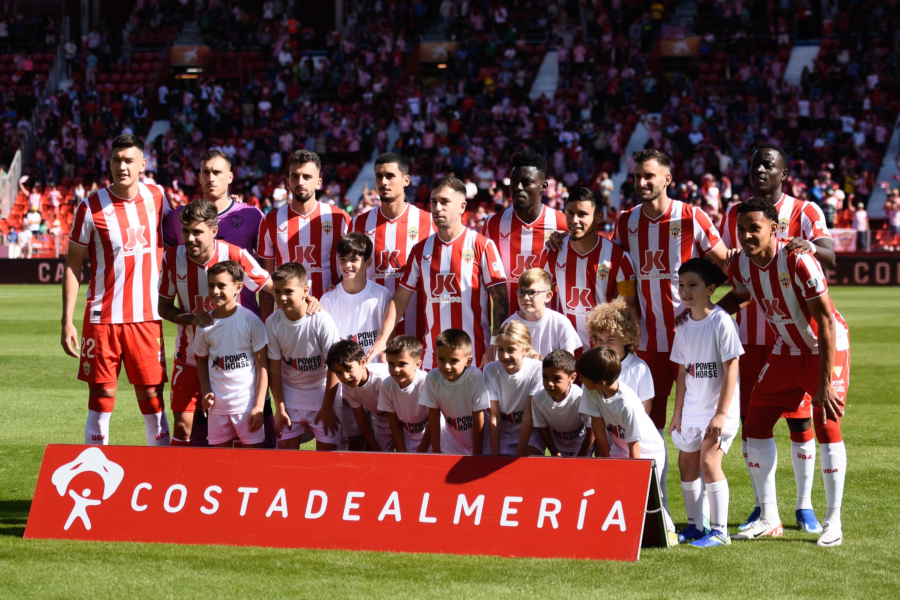 El segundo once del Almería de Gaizka Garitamo rodeado de niños luciendo la camiseta con el logo de Power Horse, patrocinador del club.