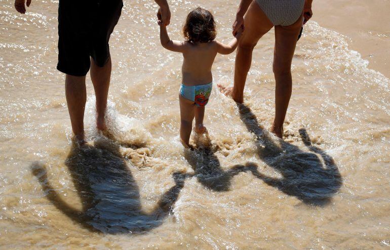 Una familia pasea por la orilla de la playa de Ondarreta de San Sebastián.