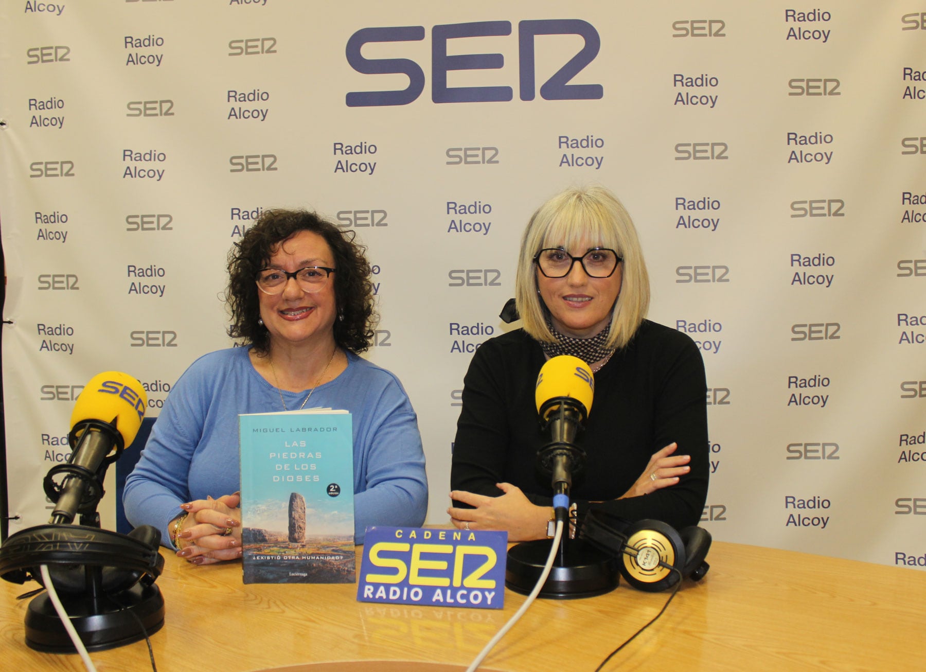 Begoña Doménech y Begoña Beneito, en el estudio central de Radio Alcoy con un ejemplar del libro &#039;Las piedras de los dioses&#039;