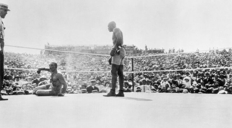 Jack Johnson de pie en el cuadrilátero frente a su rival, el blanco Jim Jeffries, totalmente noqueado.