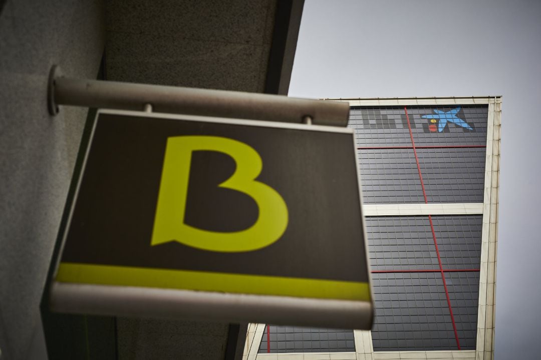 Un cartel con el símbolo de Bankia delante del logo de Caixabank tras su sustitución por el de Bankia en las torres Kio, en Madrid (España).