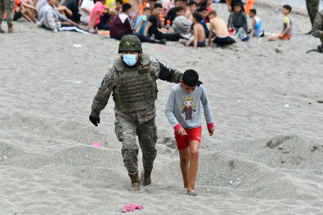 Un soldado español acompaña a un niño para volver a cruzar la frontera de vuelta a su país