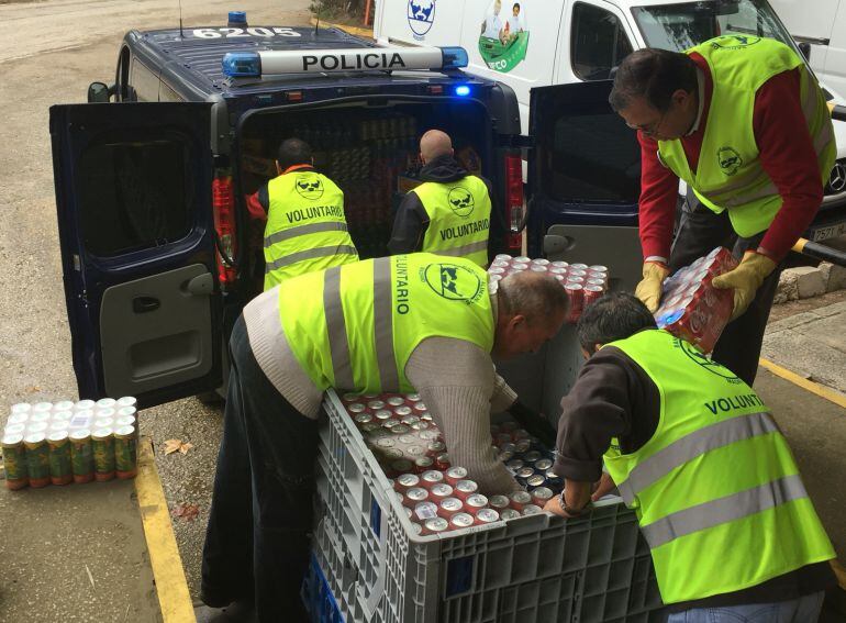 Voluntarios del Banco de Alimentos descargan cajas de bebida del furgón de la Policía.