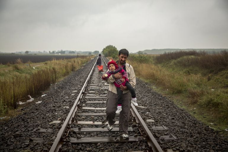 Fotografía facilitada por la Casa del Lector, realizada por el fotoperiodista Olmo Calvo, de un padre que camina por las vías del tren llevando a su hijo en brazos unos cientos de metros despues de haber cruzado la frontera entre Serbia y Hungría