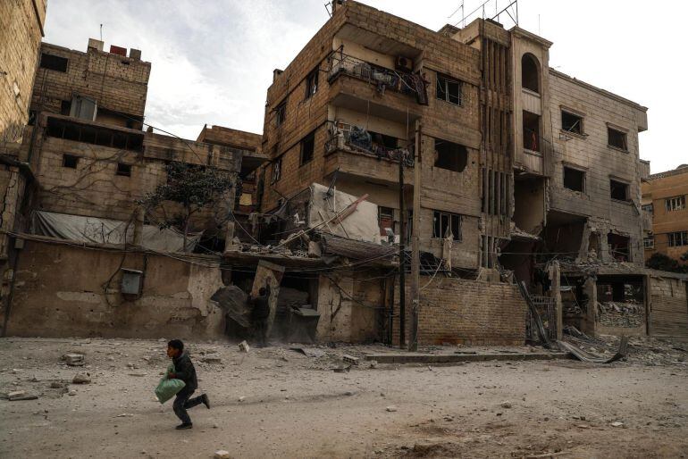 Un niño corre junto a edificios derruidos después de un bombardeo en Duma, Guta Oriental (Siria)