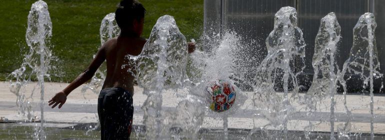 Un niño juega con una pelota en una fuente pública