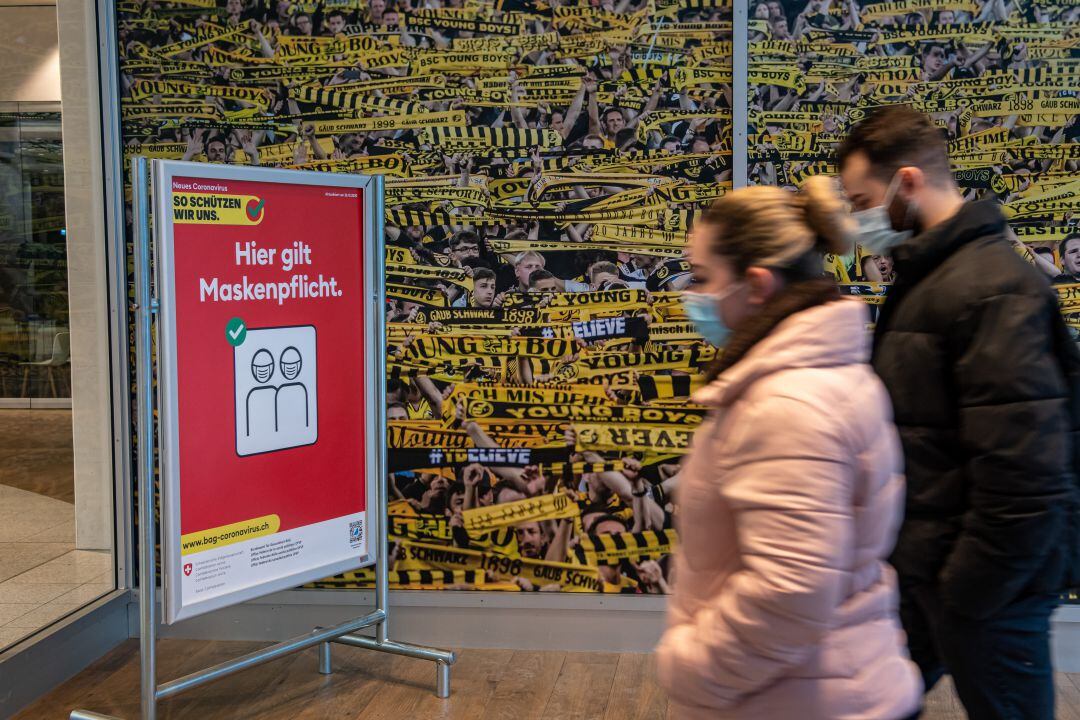 Dos trabajadores entrando en el estadio del Young Boys, en Berna (Suiza) junto a un cartel que indica que la mascarilla es obligatoria