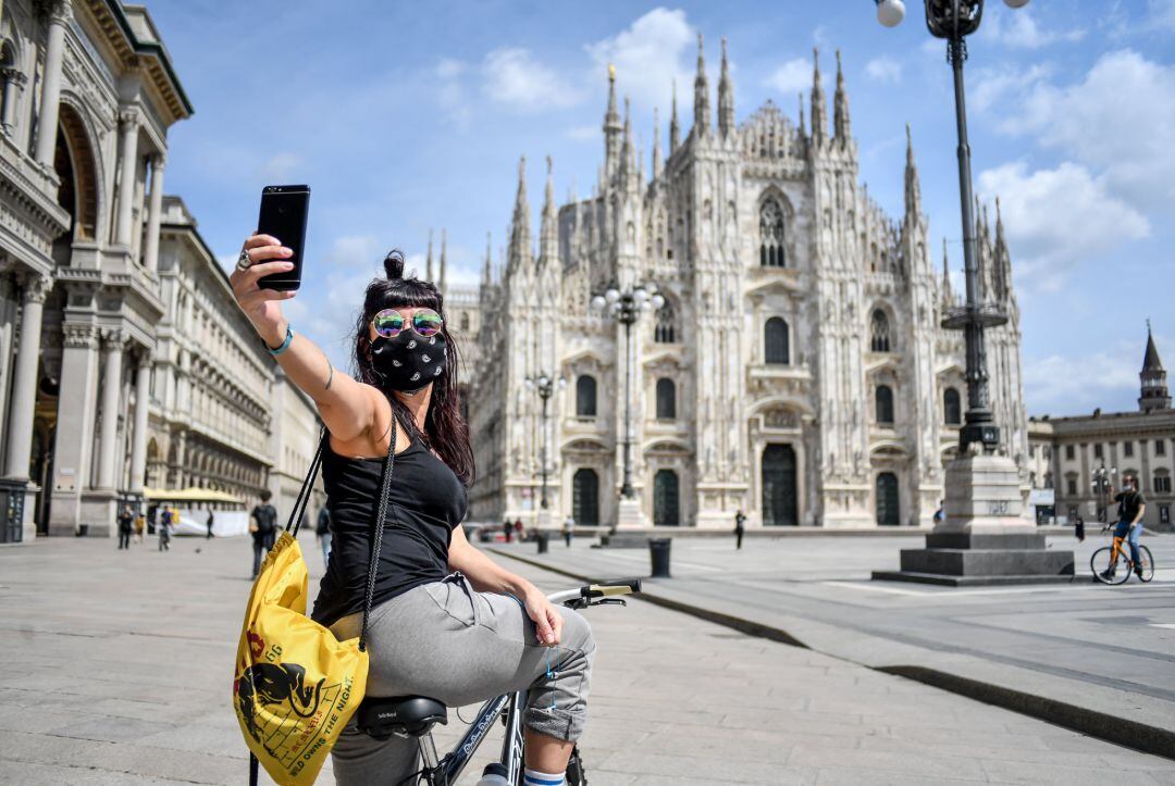 Una mujer con mascarilla se hace un selfie frente a la catedral de Milán.