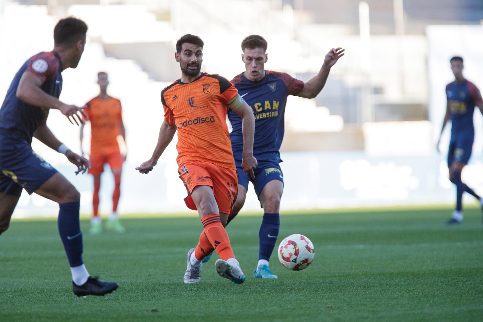 Adri Rodríguez golpea el balón perseguido por un jugador del UCAM Murcia