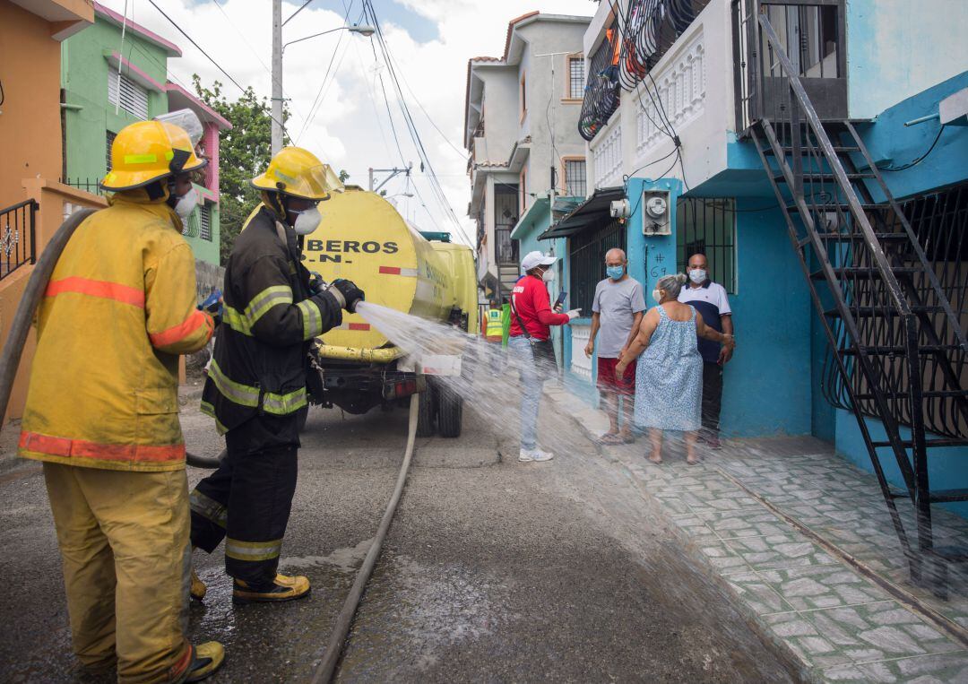 Los trabajadores municipales y los bomberos fumigan y desinfectan una calle cercana a los residentes como medida preventiva contra el coronavirus COVID-19 en Santo Domingo