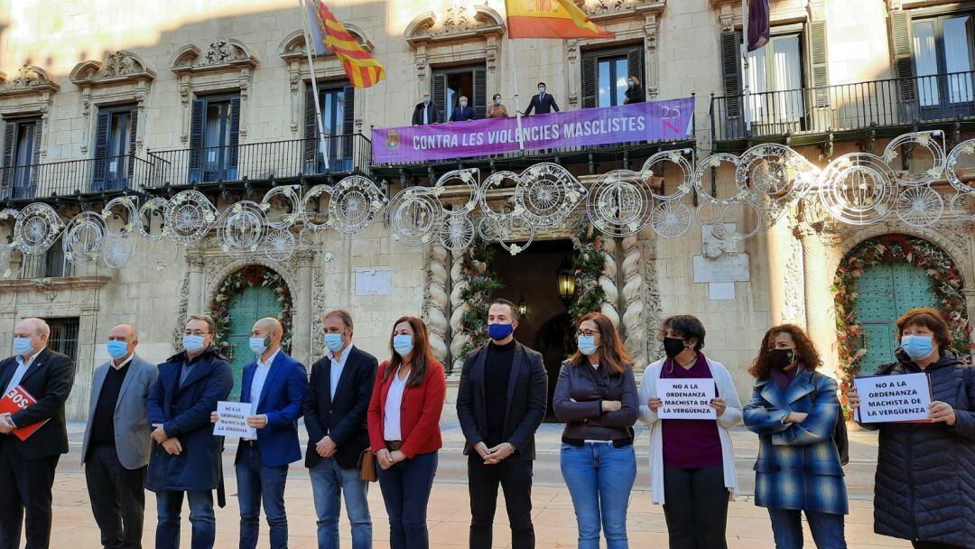 El alcalde y miembros del bipartito en el balcón del Ayuntamiento con la pancarta conmemorativa por el 25N y los ediles de la opsoción progresista en la calle, como protesta por la aprobación de la ordenanza contra la mendicidad y prostitución.