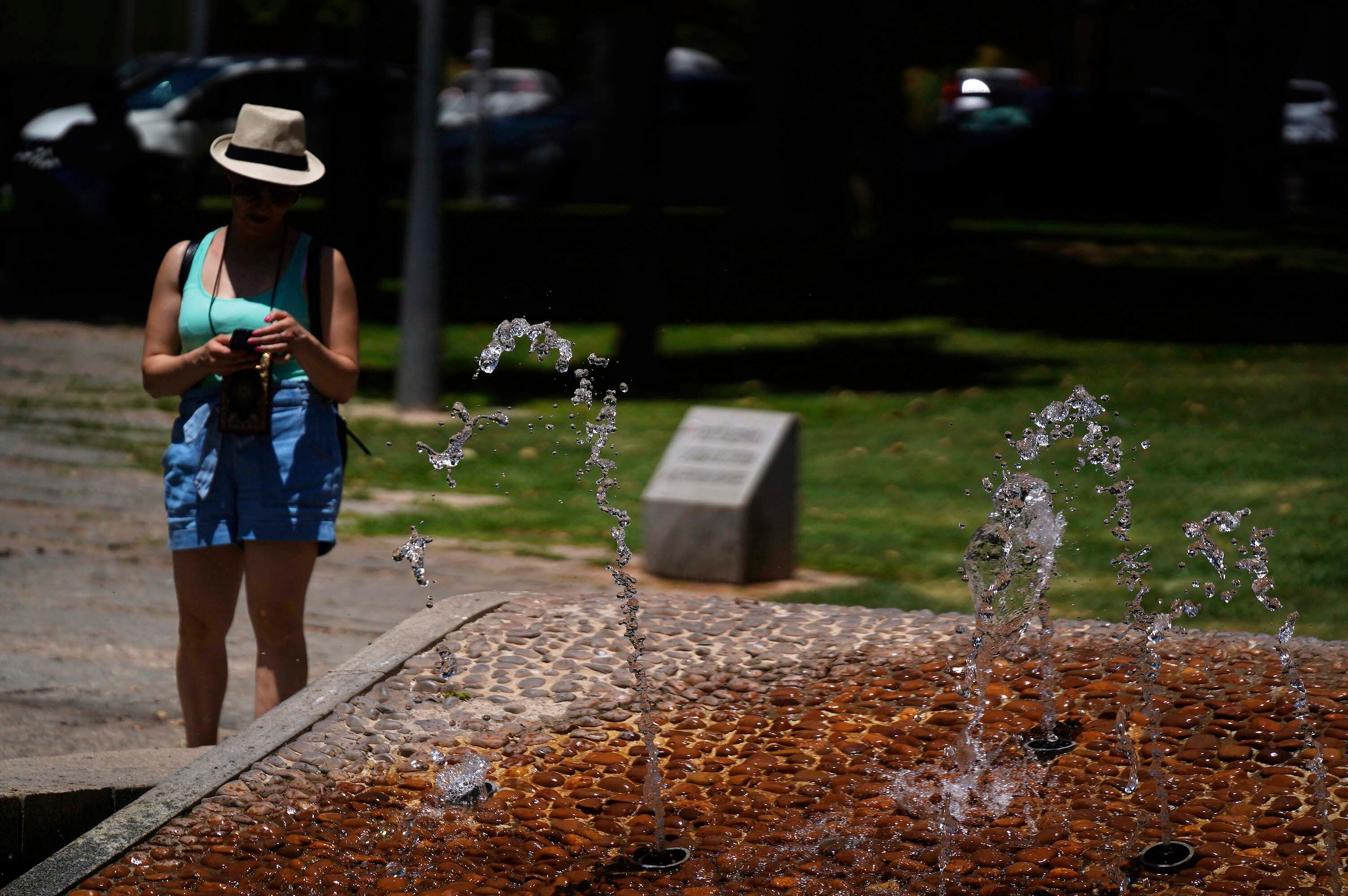 CÓRDOBA, 11/06/2022.- Una mujer pasa junto a una fuente protegida de las altas temperaturas con un sombrero, este sábado en Córdoba. La Aemet ha informado de que desde mañana empieza un episodio de ola de calor y las temperaturas máximas es "muy probable" que lleguen a 34-36 grados de forma bastante generalizada en el interior peninsular y Mallorca; aunque podrían alcanzar entre 40 y 43 grados en el valle del Guadalquivir. EFE/Rafa Alcaide